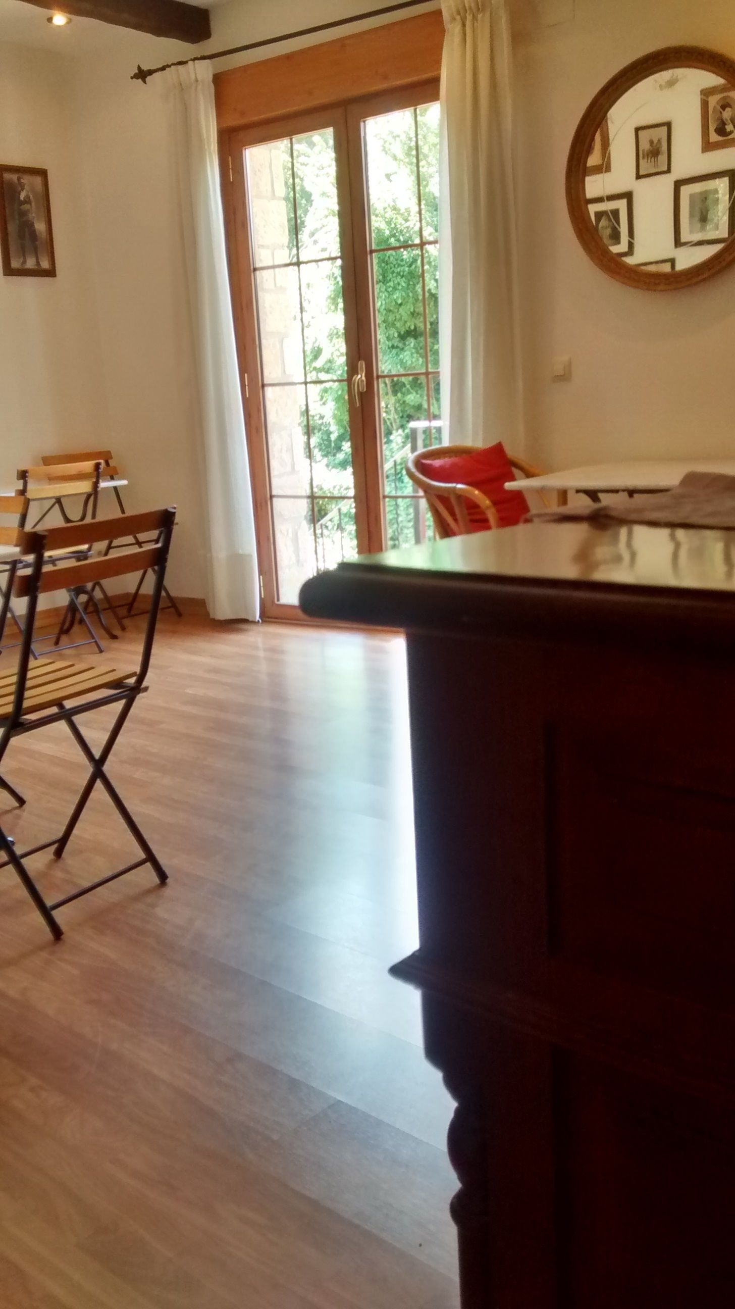 Una habitación con piso de madera, una mesa de comedor con sillas, un ventanal con cortinas y un espejo en la pared.