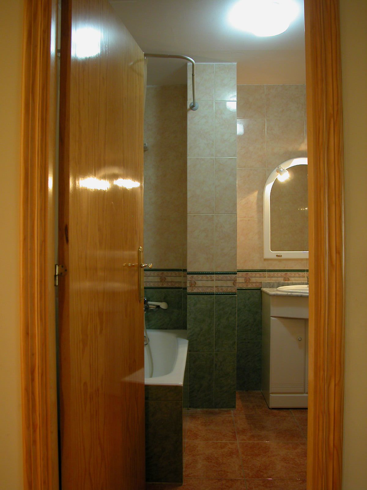 A bathroom with a wooden door, a shower, a sink, and a toilet.
