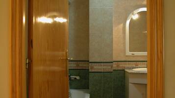 A bathroom with a wooden door, a shower, a sink, and a toilet.