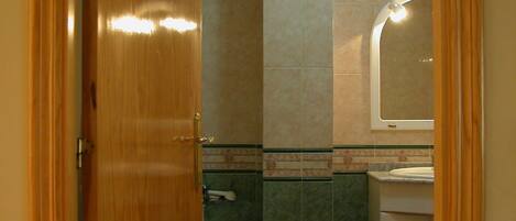 A bathroom with a wooden door, a shower, a sink, and a toilet.