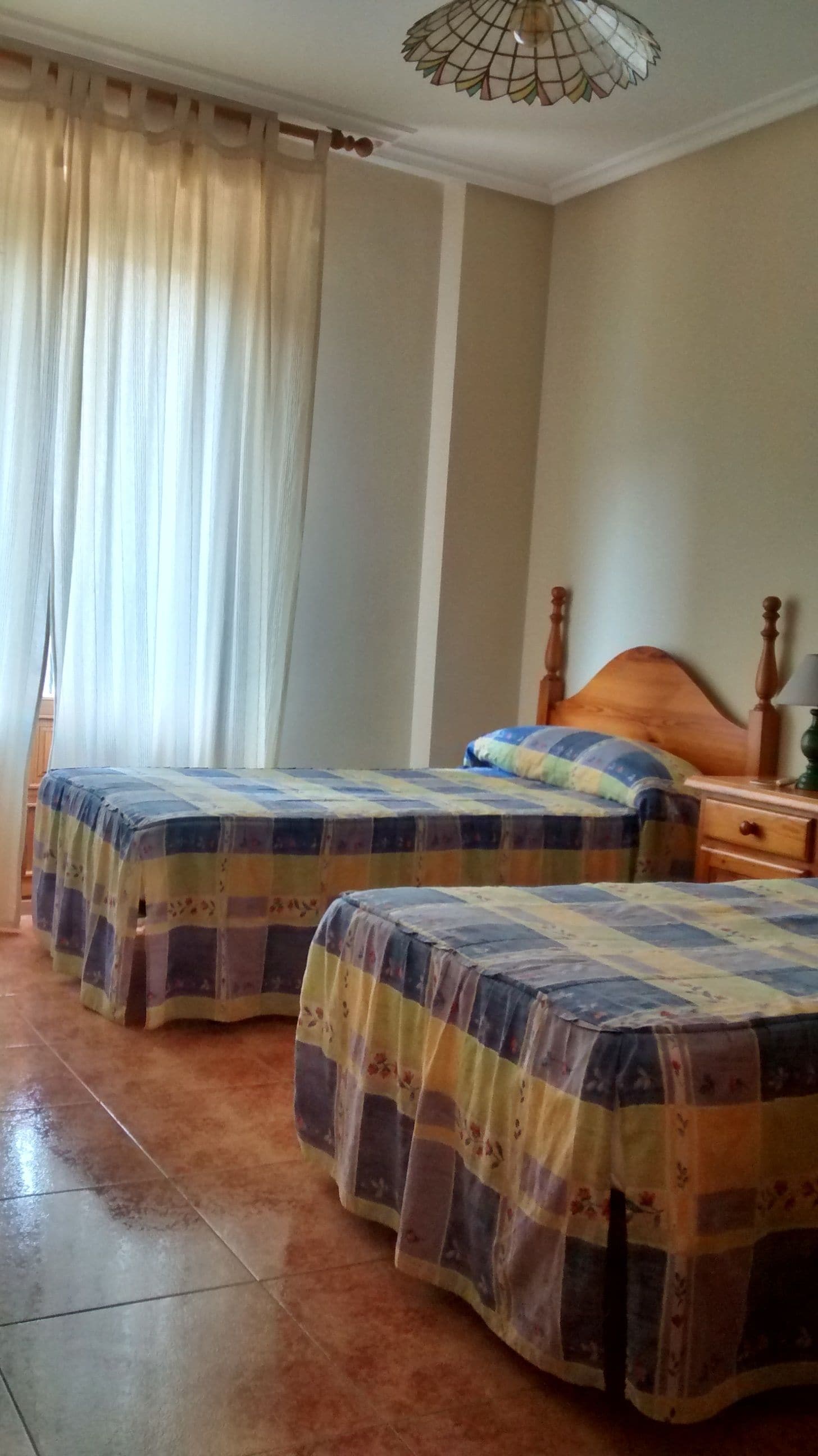 Un dormitorio con dos camas, cabecera de madera, mesita de noche y lámpara colgante.