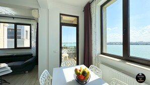 Una habitación moderna con balcón, una mesa de comedor con frutero y vistas al agua y al paisaje urbano.
