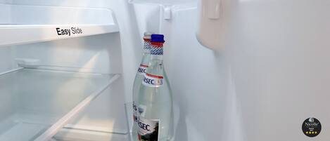 An open refrigerator with a bottle of water on the door shelf.