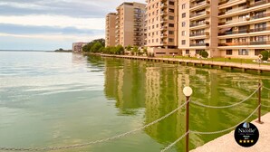 Un edificio residencial frente al agua con varios balcones, una vista despejada del mar y una barrera de cadena a lo largo de la orilla.