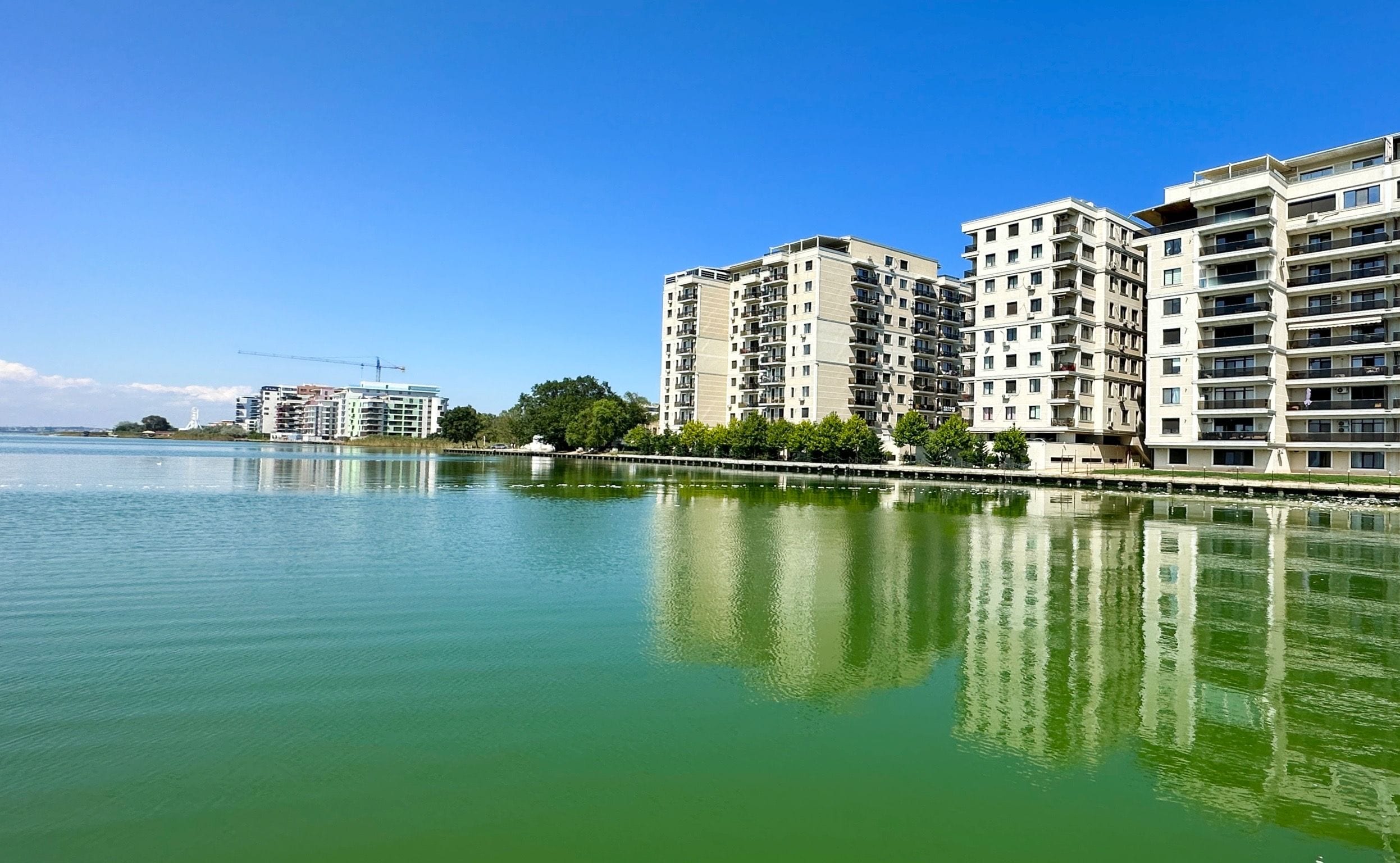 A waterfront residential area with modern apartment buildings, a calm river, and a clear blue sky.