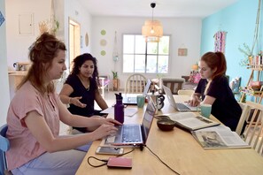 A group of people working at a wooden table with laptops, books, and a coffee mug. - The White Hill Guest House - Hostel (Ramat Negev)