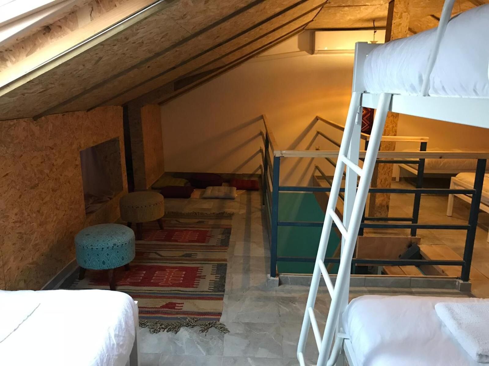 Habitación tipo dormitorio con literas, una escalera, un pequeño taburete y una alfombra estampada.