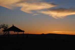 A silhouette of a thatched-roof structure against a sunset sky. - The White Hill Guest House - Hostel (Ramat Negev)