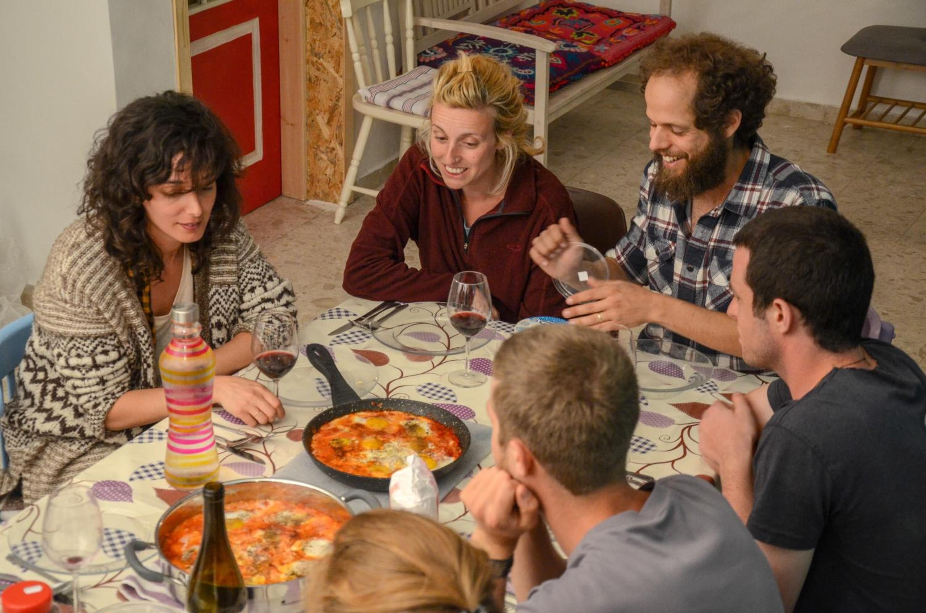 Un grupo de personas sentadas alrededor de una mesa con comida, incluyendo una fuente de comida y botellas de vino.
