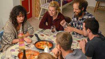 Un grupo de personas sentadas alrededor de una mesa con comida, incluyendo una fuente de comida y botellas de vino.