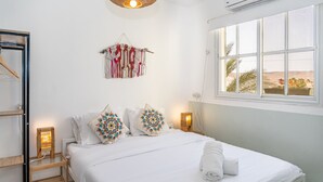Un dormitorio con cama, mesitas de noche, un adorno colgante de macramé y una ventana con vistas.