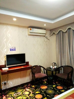 A hotel room with a flat-screen TV, two chairs, a small table with a coffee maker, and an air conditioning unit on the wall. - Jiazhou Hotel (Foshan)