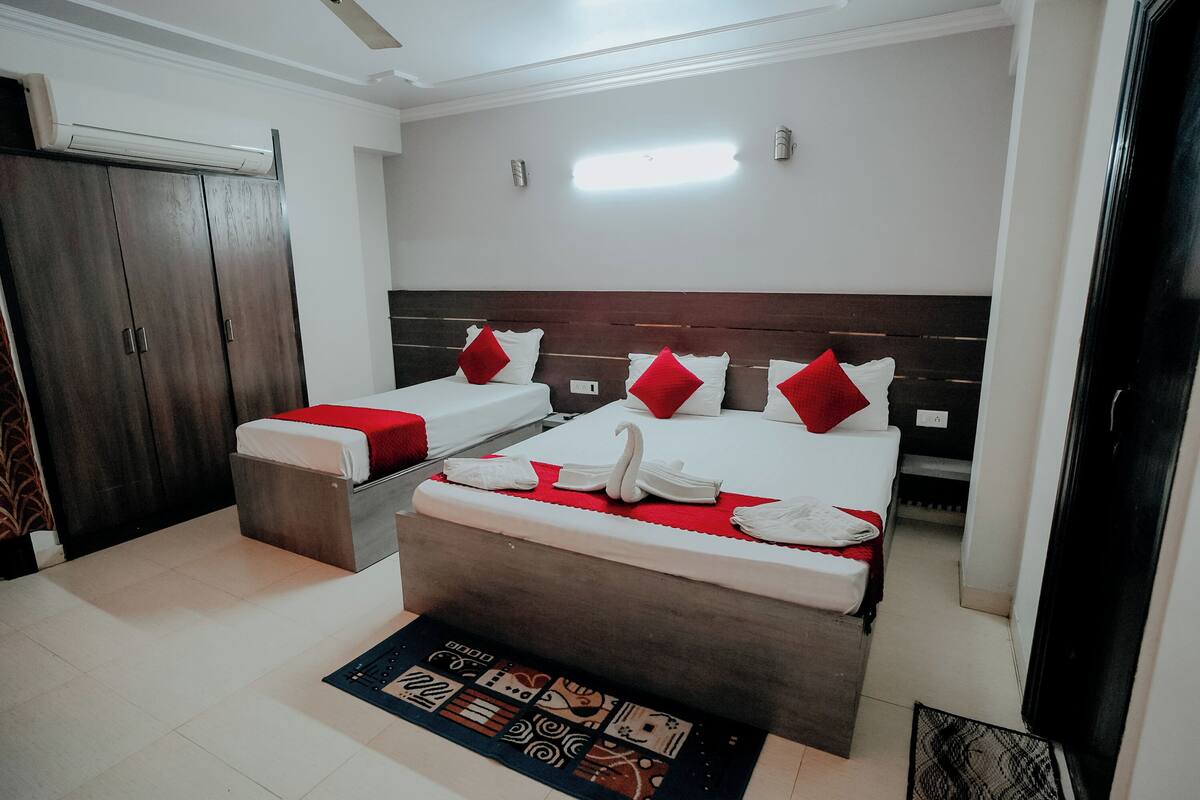 A hotel room with two single beds, a large bed, a wardrobe, and a small table.