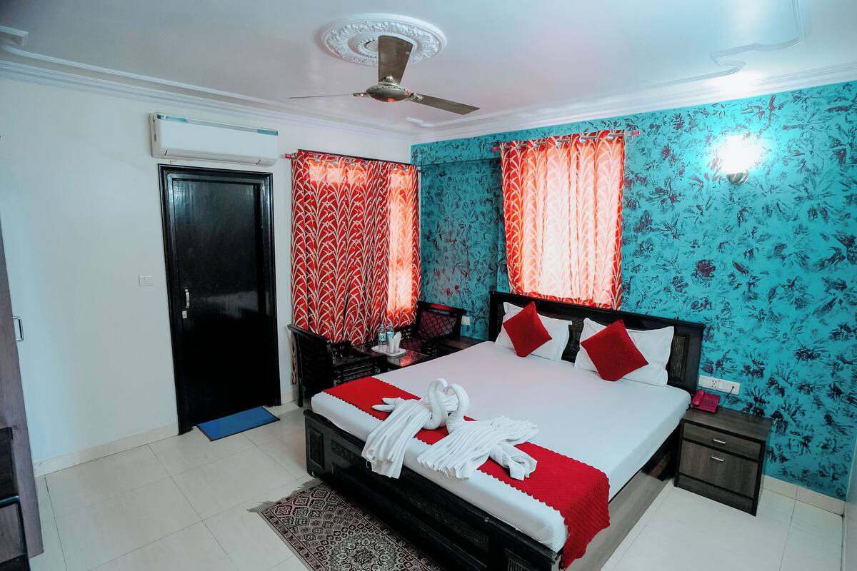 A hotel room with a bed, a nightstand, a desk, a chair, a door, and a ceiling fan.