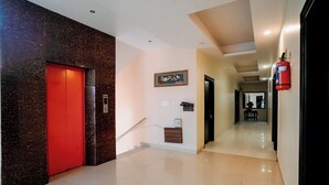 Pasillo de hotel con un ascensor rojo, una escalera, un extintor y un cuadro en la pared.