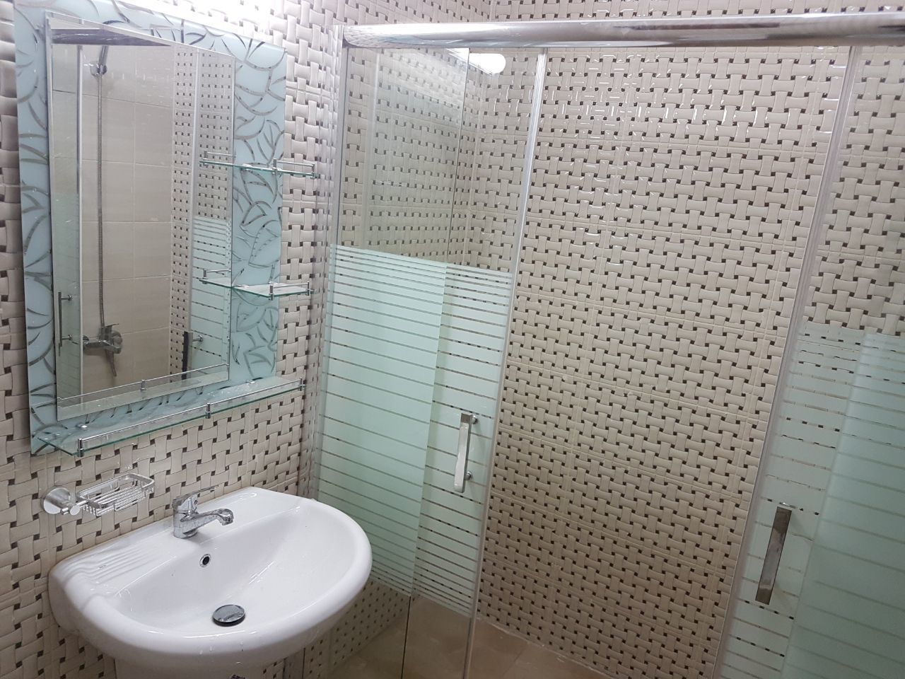 A bathroom with a glass shower enclosure, a sink with a mirror, and a patterned wall.