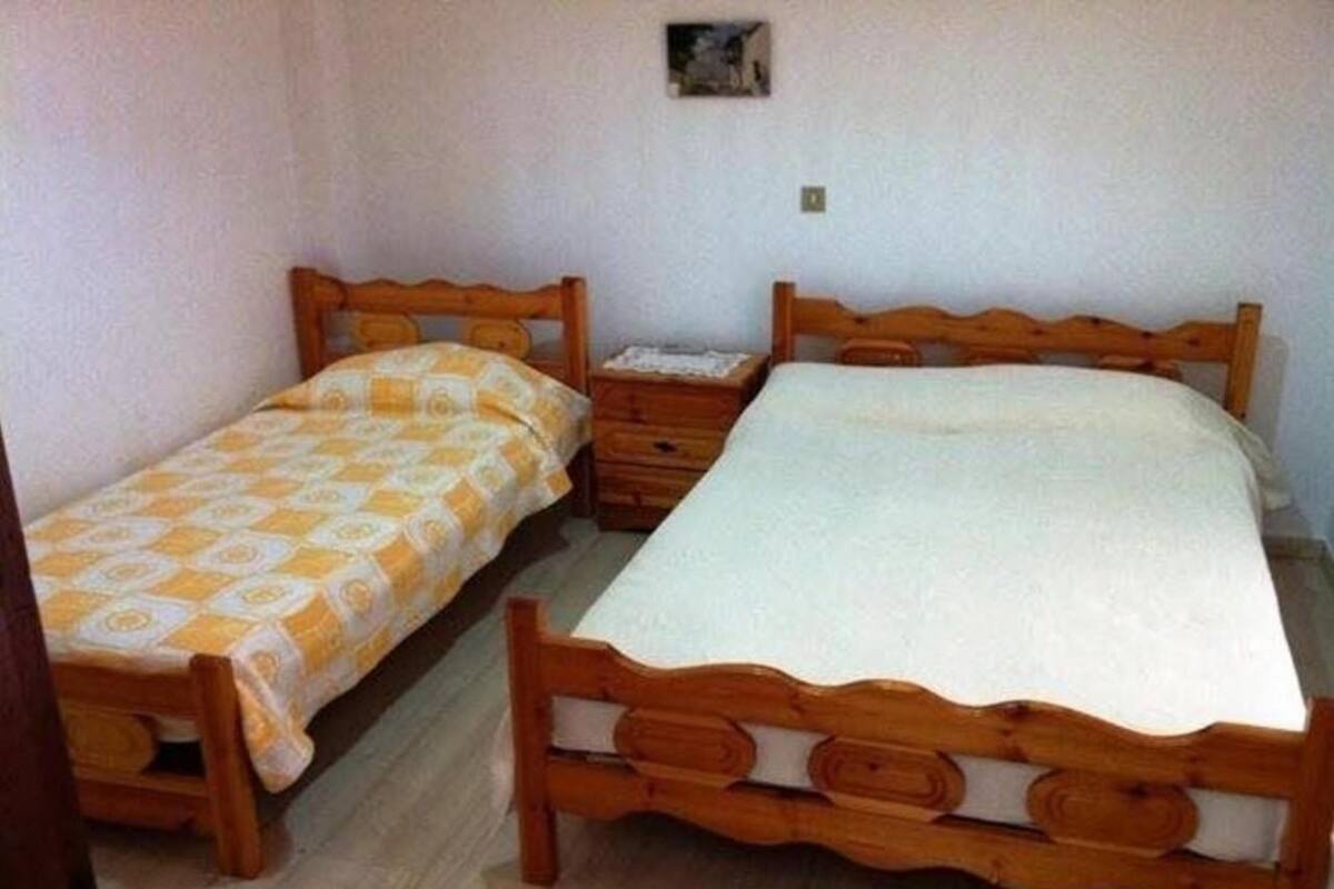 Een kamer met twee houten bedden, waarvan er één een beddengoed met een patroon heeft en de ander een effen.
