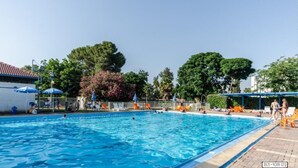 Une piscine à l’eau d’un bleu limpide, entourée d’arbres et de parasols.