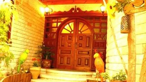 Une porte en bois surmontée d’une arche décorative, des plantes en pot et une statue d’oiseau au premier plan.
