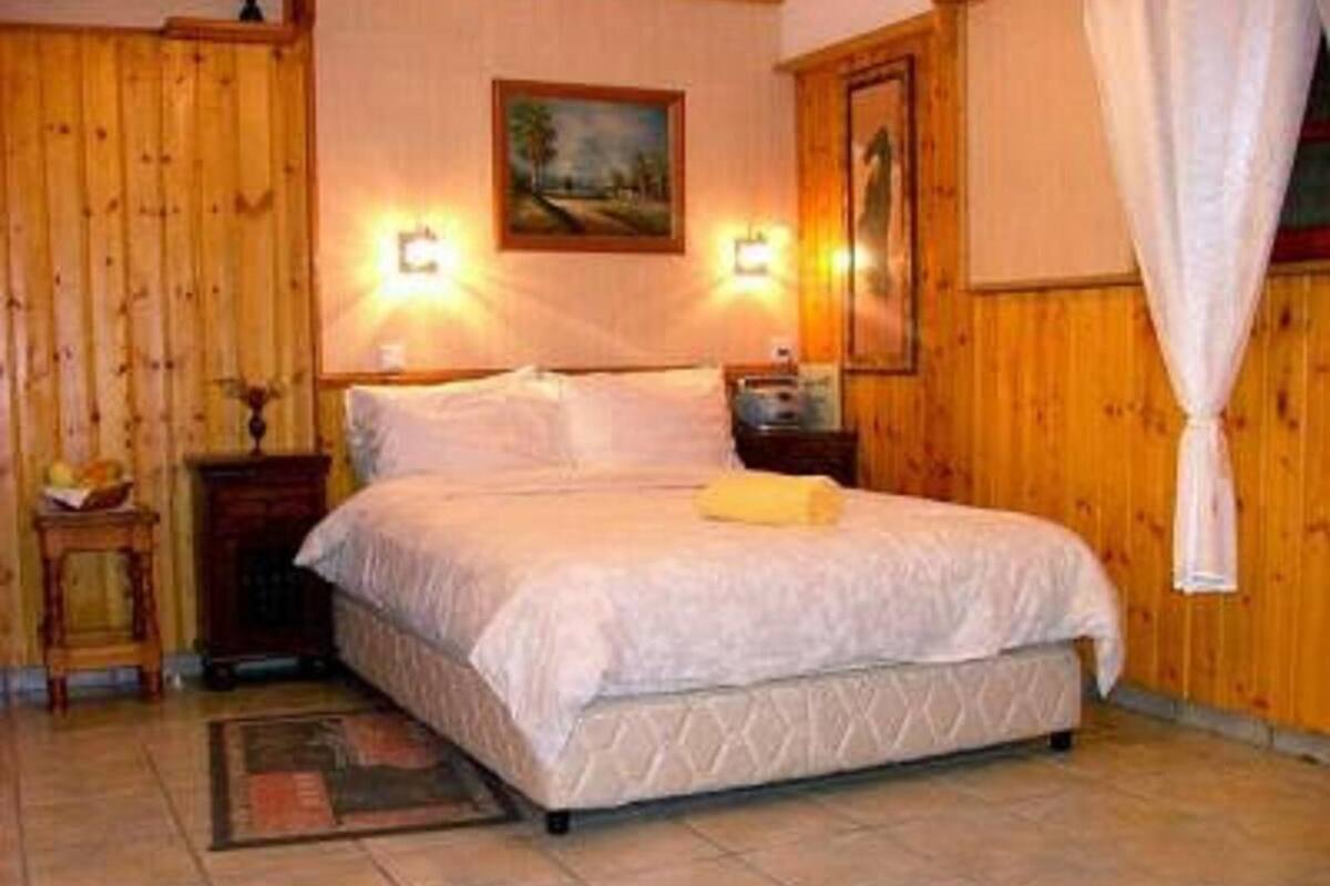 A bedroom with a large bed, wooden walls, two bedside tables, and a painting on the wall.