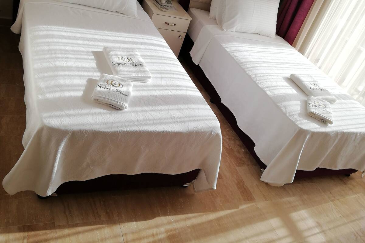 Two neatly made beds with white linens and towels, a bedside telephone, and a wooden floor.