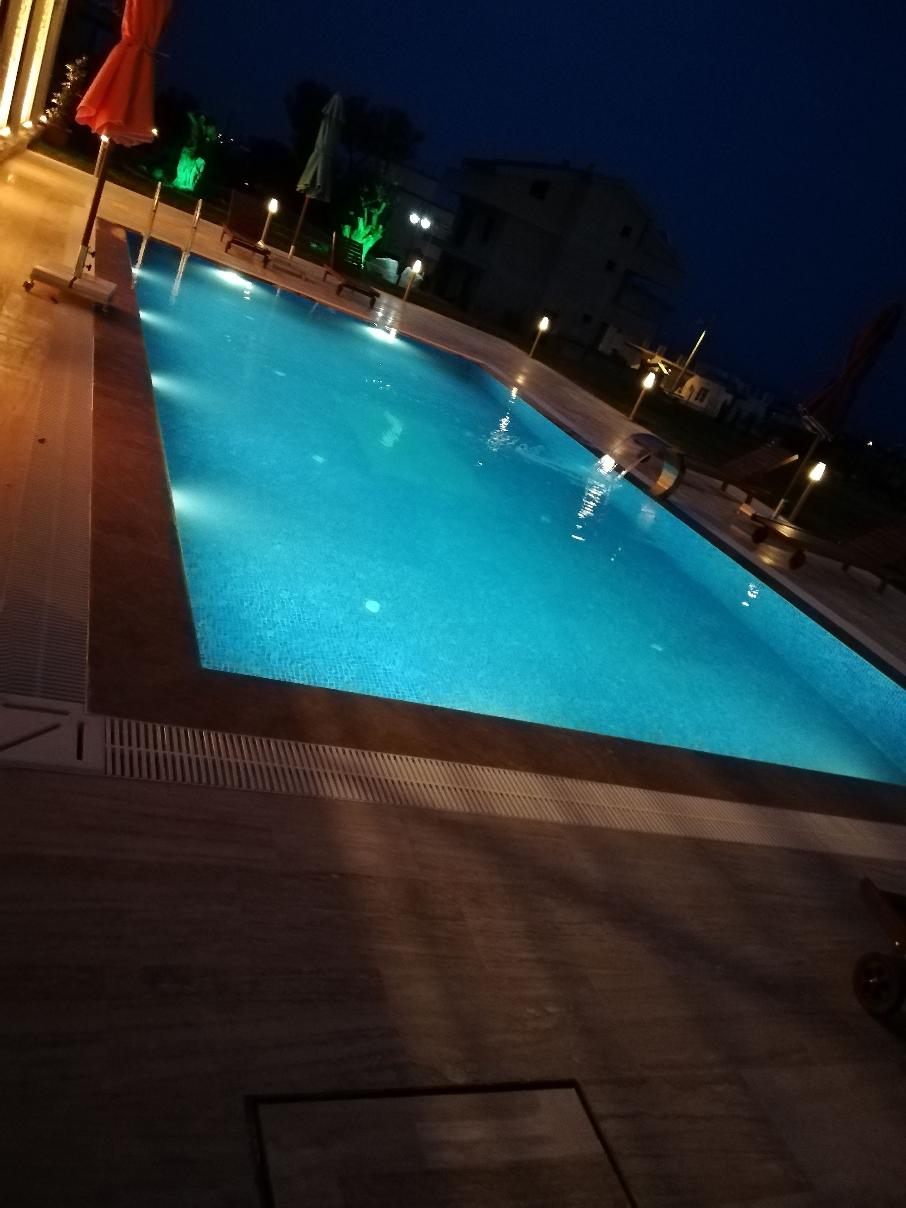 A swimming pool at night with surrounding lounge chairs and umbrellas.