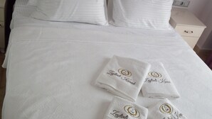 Una cama bien hecha con sábanas blancas y cuatro toallas con bordados.