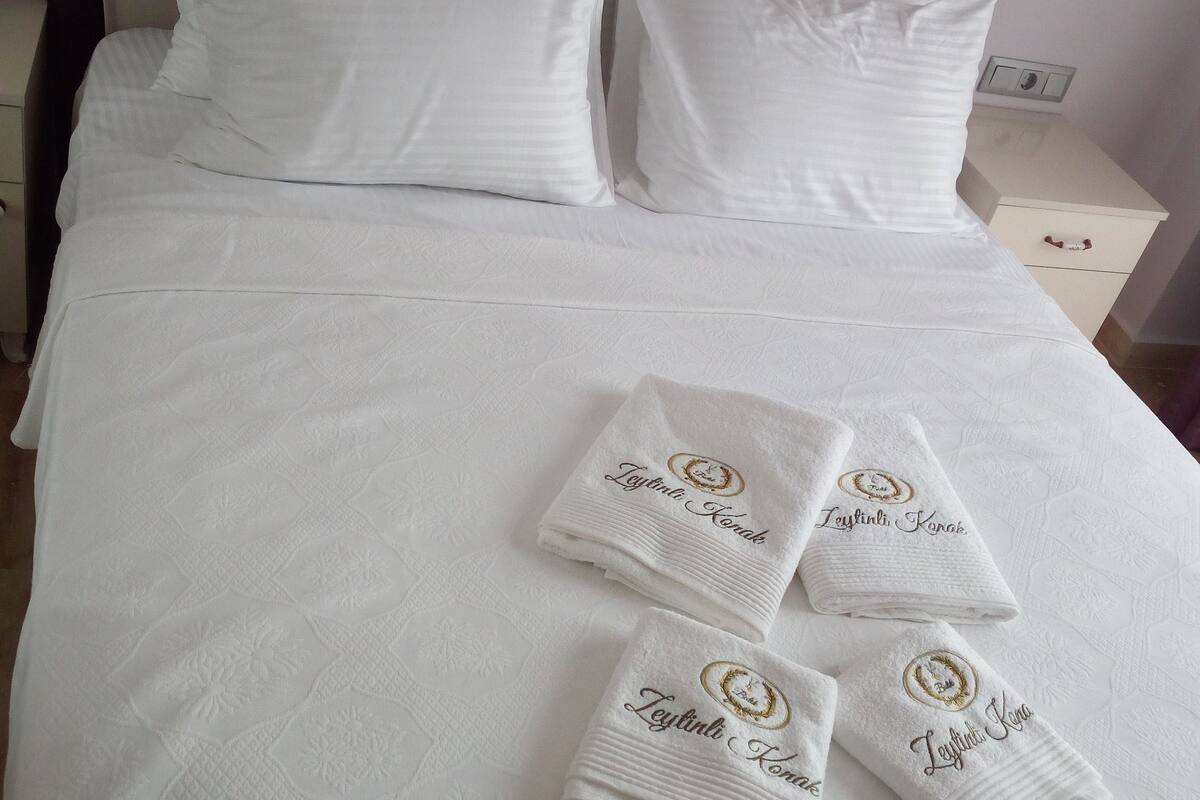 A neatly made bed with white linens and four towels with embroidered text.