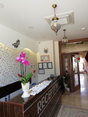 A reception area with a wooden reception desk, a vase with pink orchids, framed certificates on the wall, and a ceiling fan. - MORDOĞAN Zeytinli Konak Butik Hotel (Karaburun)