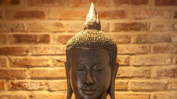 Une statue de Bouddha, placée sur un meuble rouge, se dresse devant un mur de briques.