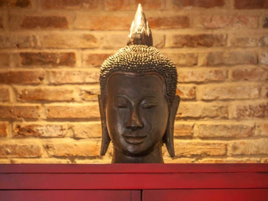 Une statue de Bouddha, placée sur un meuble rouge, se dresse devant un mur de briques.