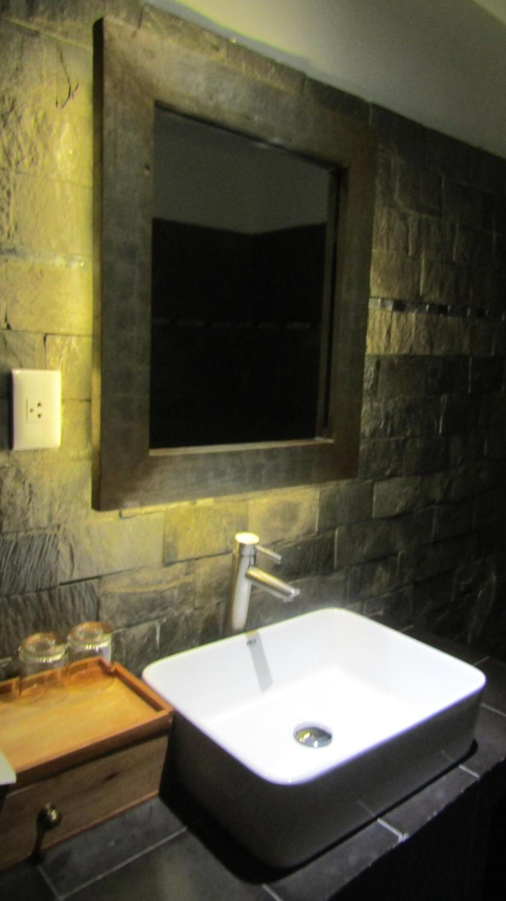 A bathroom with a stone wall, a white sink, and a mirror.