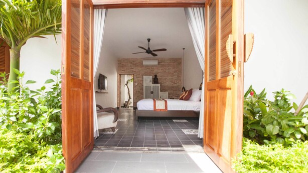 A bedroom with a bed, a ceiling fan, and a brick wall. - La Casita Saigon (Ho Chi Minh City)
