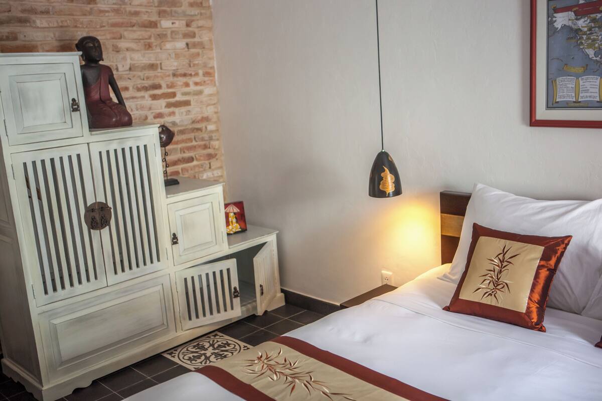 A bedroom with a bed, a nightstand, a dresser, a hanging light, and a wall map.