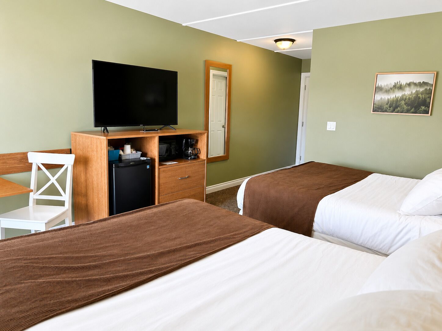Ein Hotelzimmer mit zwei Betten, einem Fernseher, einem Schreibtisch mit Stuhl, einem Kühlschrank und einer Kaffeemaschine.