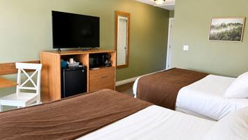Ein Hotelzimmer mit zwei Betten, einem Fernseher, einem Schreibtisch mit Stuhl, einem Kühlschrank und einer Kaffeemaschine.