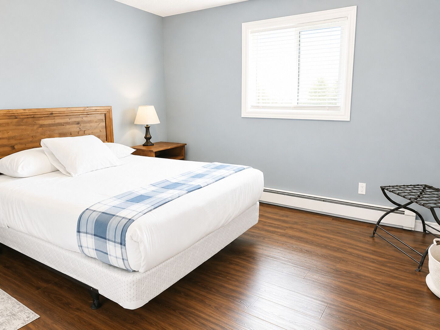Un dormitorio ordenado con cama, mesita de noche, lámpara y ventana.