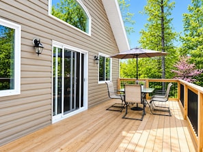 Una terraza con mesa y sillas, una puerta corrediza de vidrio y una pérgola con sombrilla.