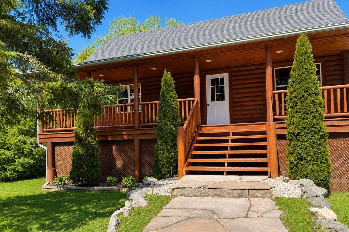 Une cabane en rondins avec un porche, des marches en pierre et une pelouse bien entretenue.