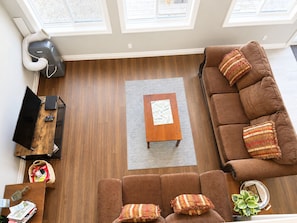 Un salon avec un canapé marron, une table basse en bois, un téléviseur et un ventilateur de plafond.