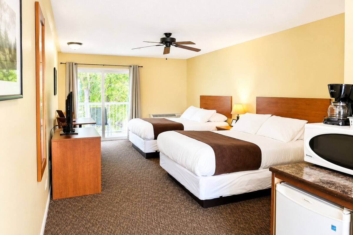 Une chambre d’hôtel avec deux lits, un ventilateur de plafond, une machine à café et un réfrigérateur.