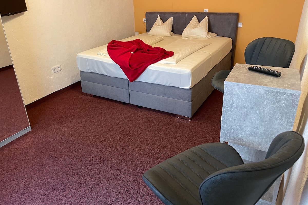 Une chambre d’hôtel équipée d’un lit, d’un bureau, d’une chaise et d’un téléviseur fixé au mur.