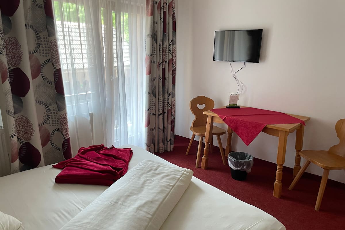 Une chambre d’hôtel avec un lit, un bureau et une chaise, un téléviseur fixé au mur et une fenêtre avec des rideaux.