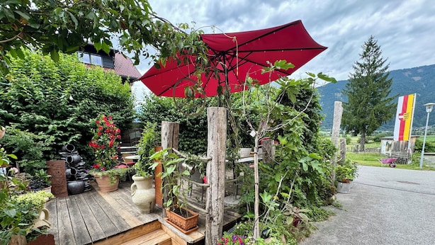 Une terrasse en bois agrémentée de plantes en pot, d’un parasol rouge et d’une structure en bois rustique.