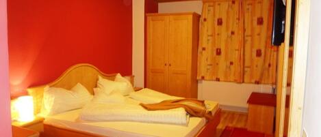 Un dormitorio con una cama de madera, una pared roja y un armario de madera.