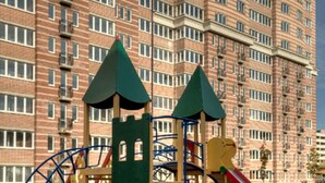 Un terrain de jeux équipé de structures d’escalade et de toboggans, avec en arrière-plan un immeuble résidentiel à plusieurs étages.