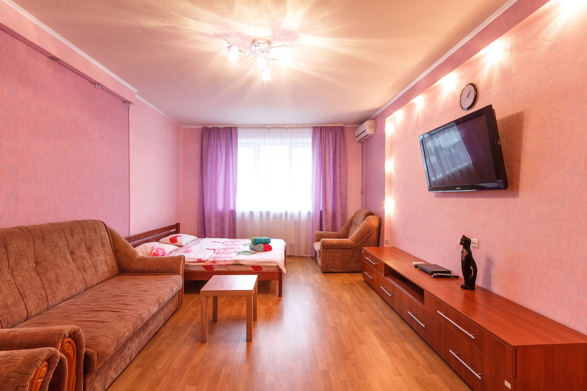 Una habitación con sofá, cama, mesa, televisor y una silla.