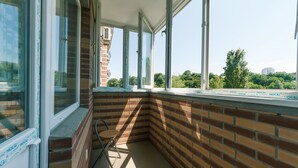 Un balcon d’angle avec des murs en briques et de grandes fenêtres donnant sur un parc et des immeubles.