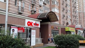 Un immeuble résidentiel à plusieurs étages doté de balcons, un commerce de détail avec une enseigne indiquant « OK wine », et un chemin piétonnier.