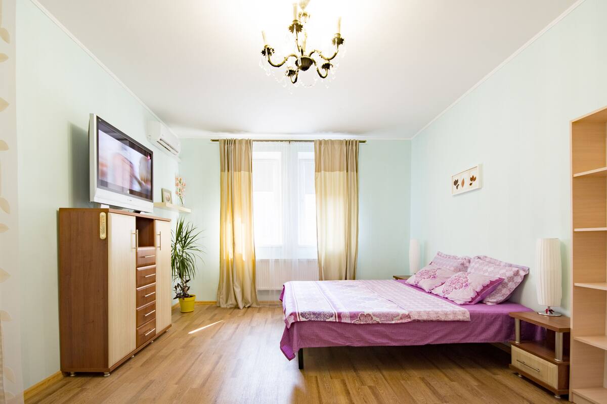 Un dormitorio con cama, armario, televisor, planta y candelabro.
